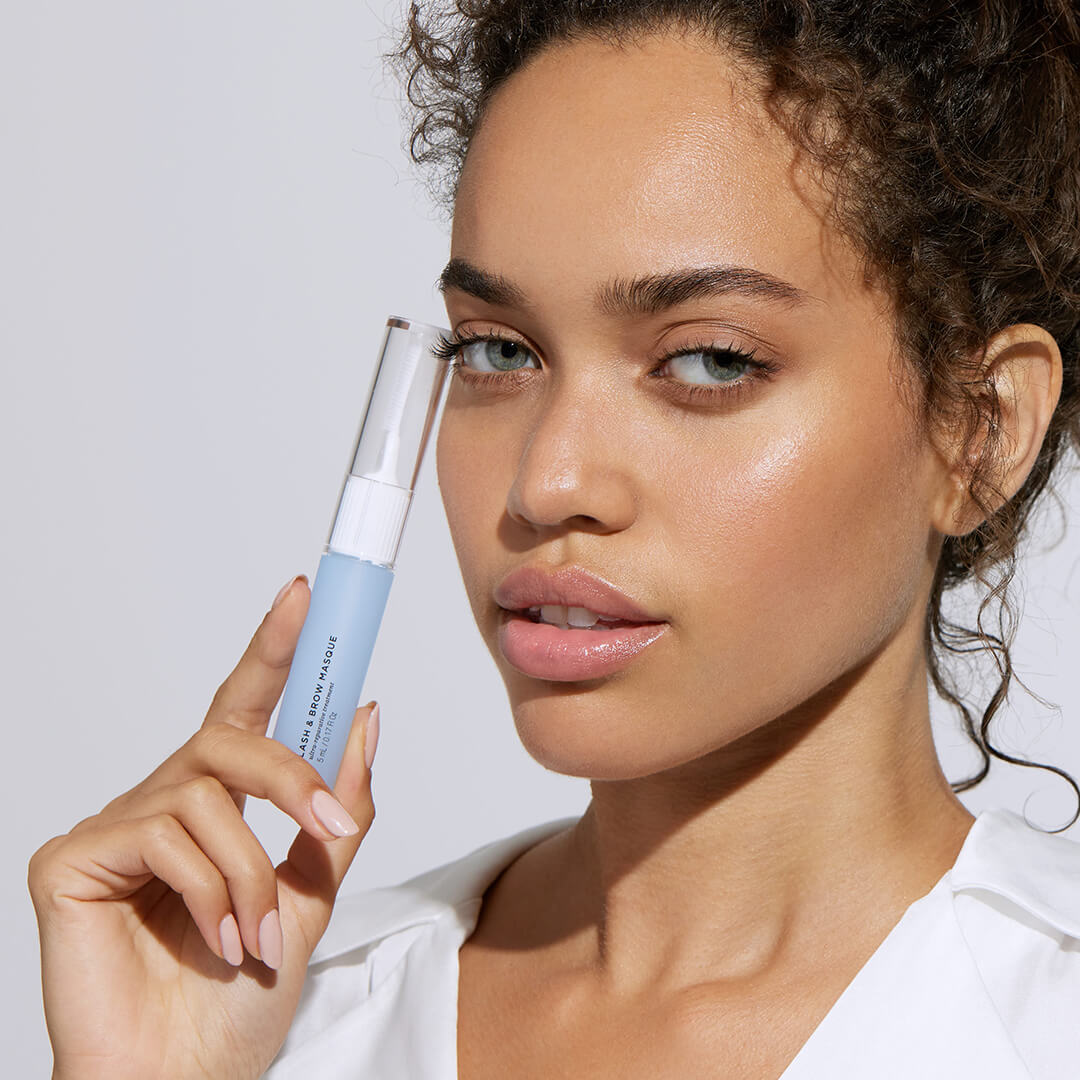 Image of model holding a tube of Lash & Brow Masque up to her face