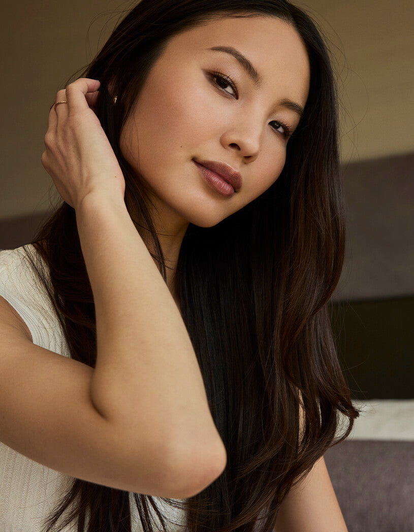 Woman with long dark hair touching her ear indoors