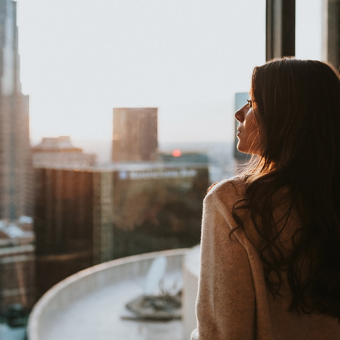 Image of woman looking outside of a window facing high rise buildings