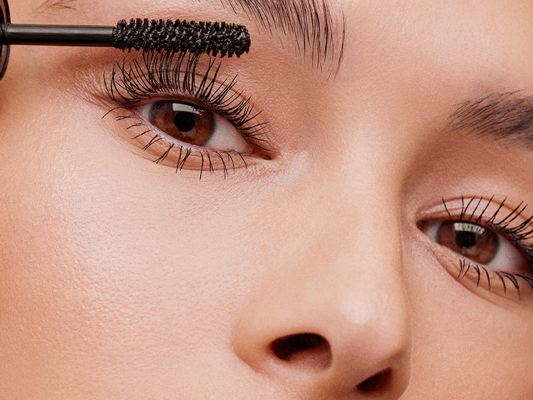 Close up image of model applying Volumizing Mascara to her eyelashes.