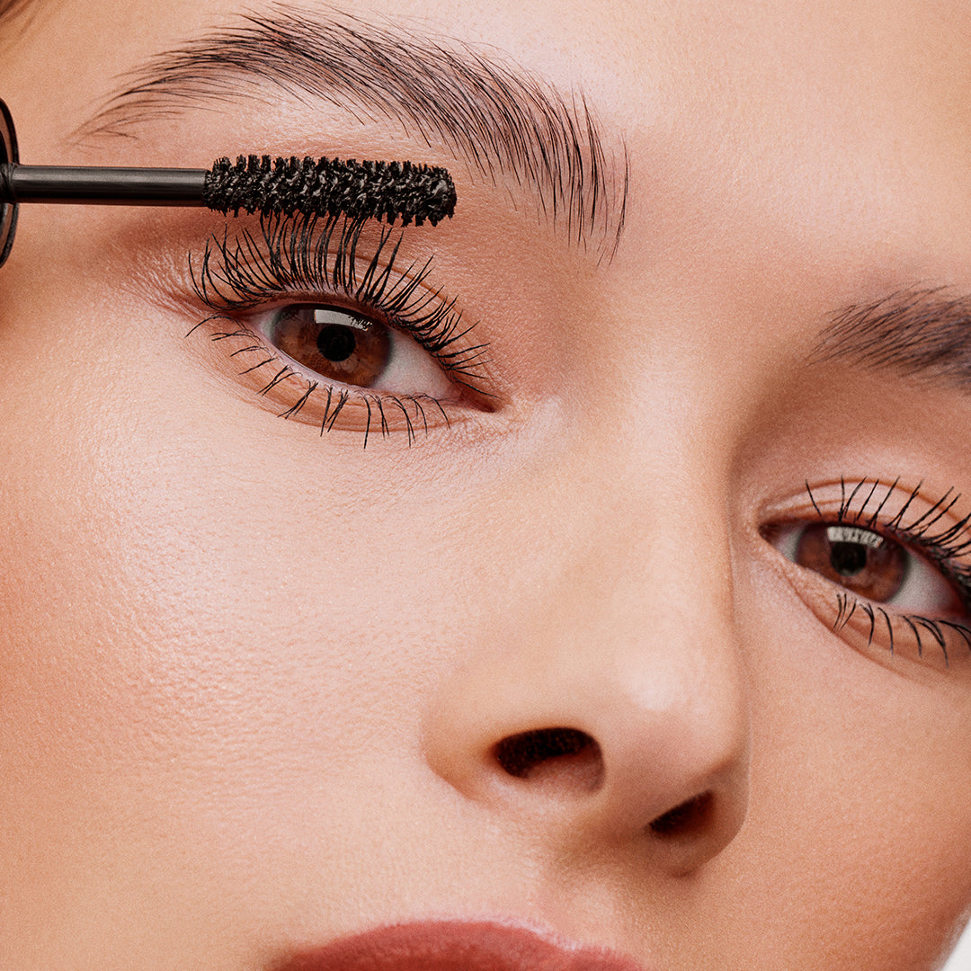 Close up image of model applying Volumizing Mascara to her eyelashes.