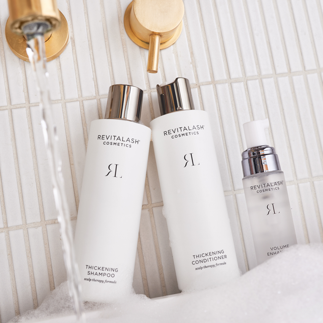 Image of Thickening Shampoo, Thickening Conditioner, and Volume Enhancing Foam sitting on the ledge of a bathtub.