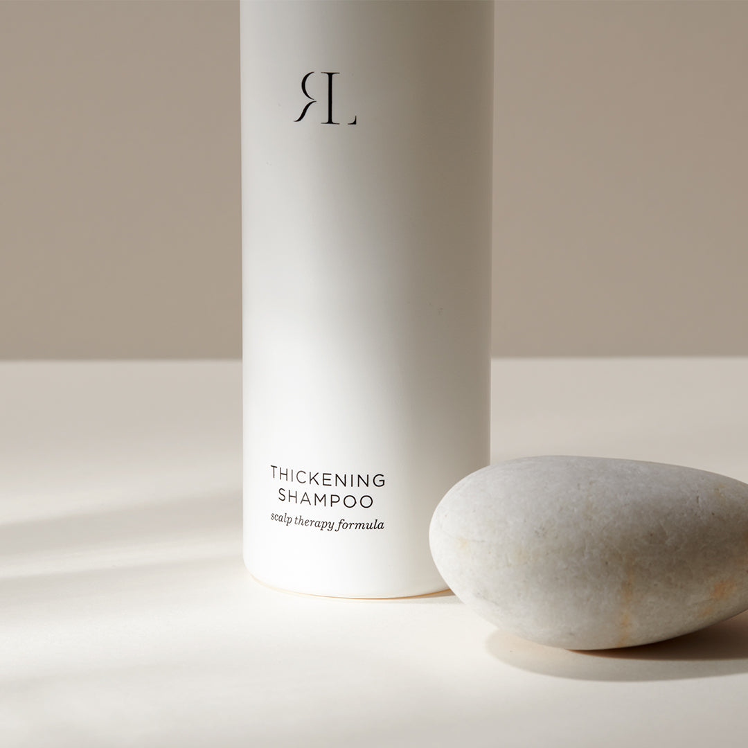 Image of a bottle of Thickening Shampoo sitting next to a small smooth rock