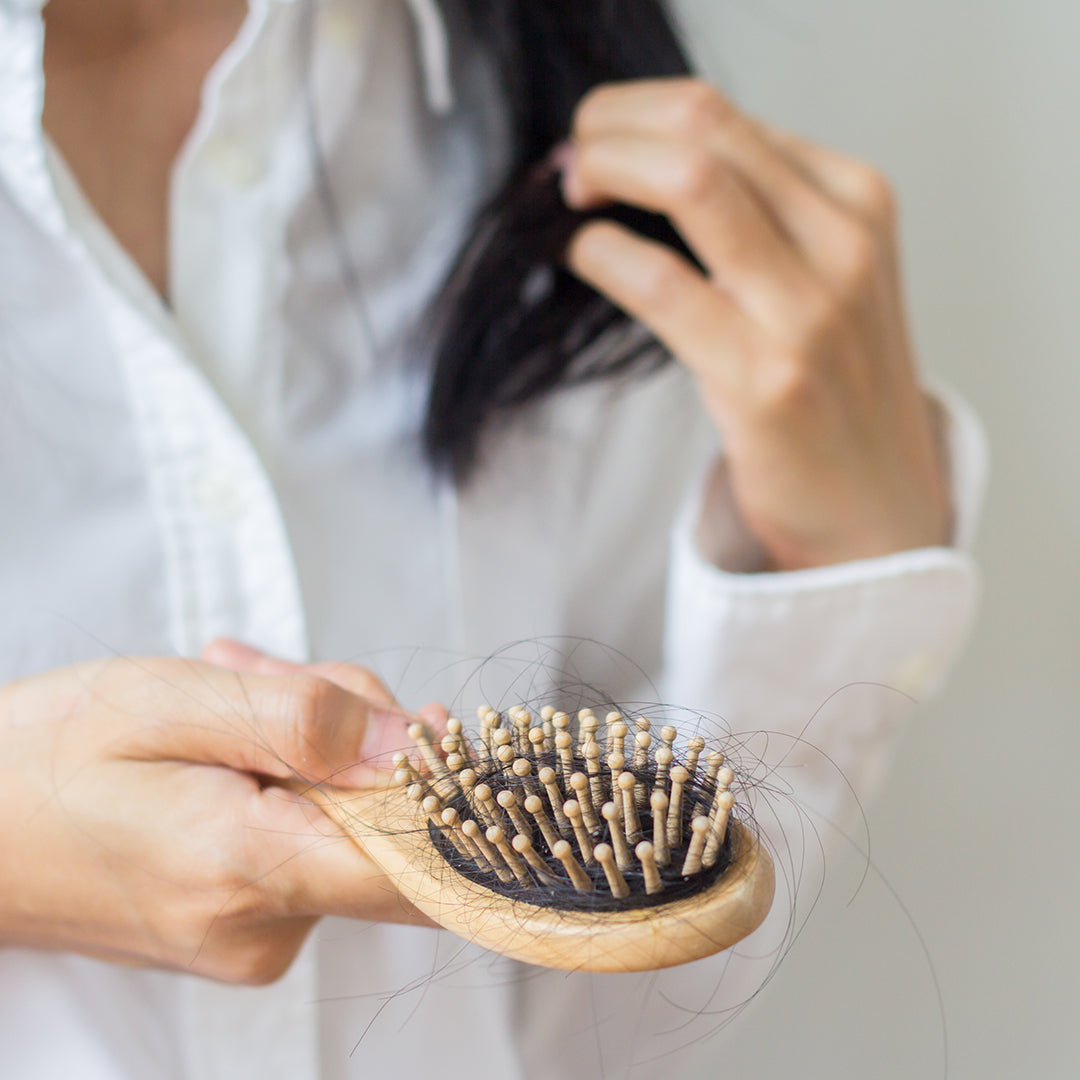 Image of woman holding a hair brush with a lot of hair clumped up in the brush