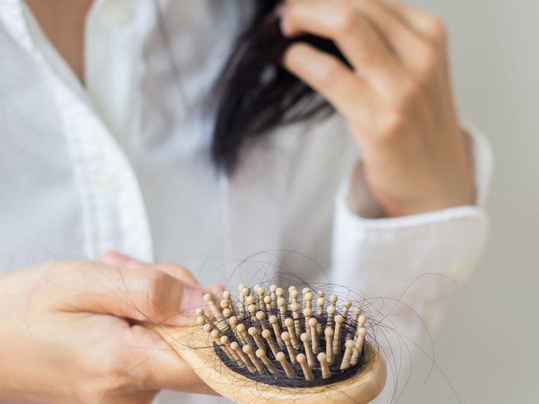 Image of woman holding a hair brush with a lot of hair clumped up in the brush