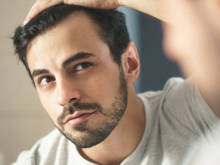 Image of man looking at hairline in the mirror