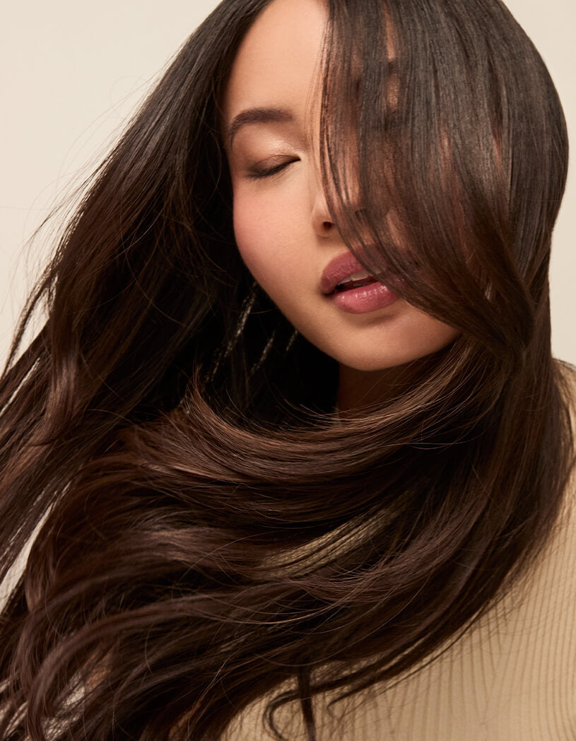 Woman with long, wavy hair covering her face against a beige background