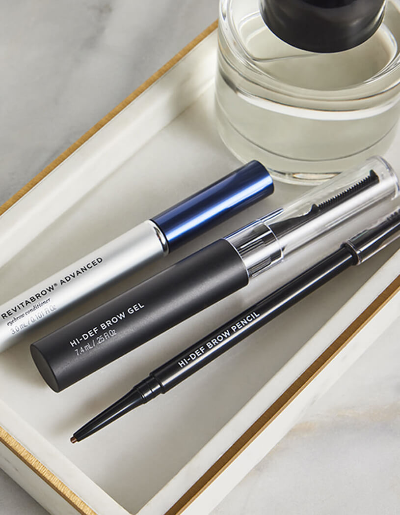 Eyebrow grooming products including a gel and pencil on a white surface.