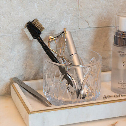 Clear glass holder with grooming tools on a marble surface
