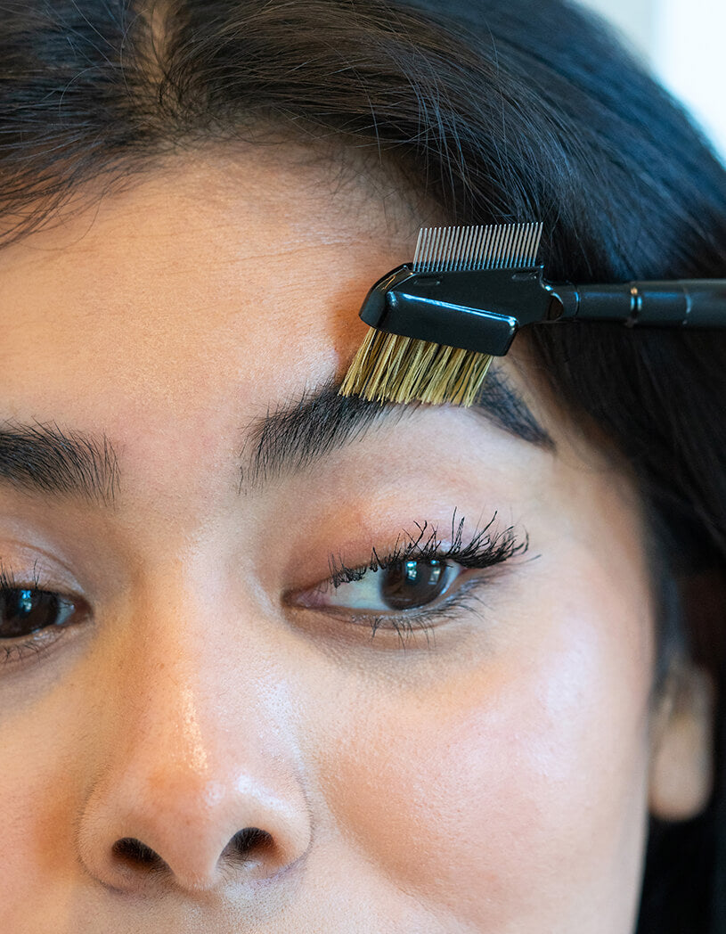 Person grooming eyebrows with a brush and comb