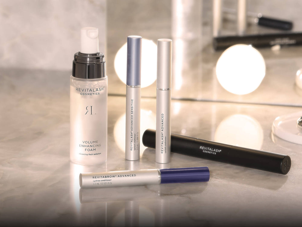 Revitalash cosmetics products on a reflective surface with a blurred mirror background. 25% off sitewide $100 purchase.